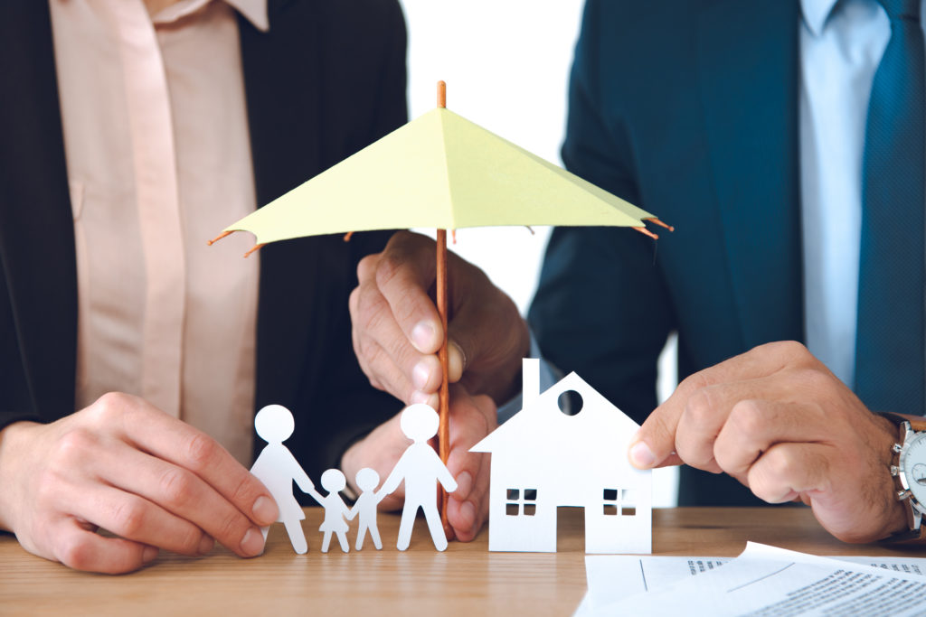 partial view of insurance agents covering family and house paper models with umbrella at workplace